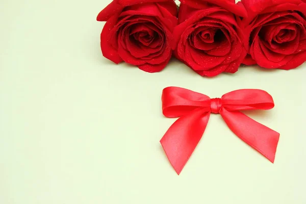 Τρία κόκκινα τριαντάφυλλα με σταγόνες νερού και ένα κόκκινο τόξο δίπλα του. Καλή κάρτα γενεθλίων. — Φωτογραφία Αρχείου