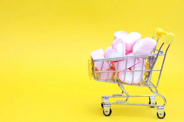 En leksaksvagn från snabbköpet är fylld med marshmallows i form av hjärtan. Gul bakgrund. Begreppet kärlek och Alla hjärtans dag. — Stockfoto