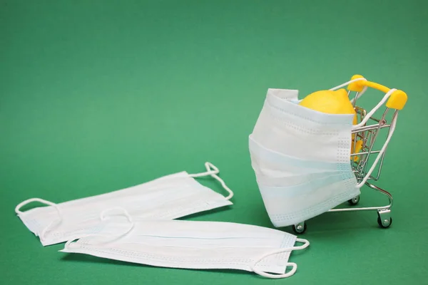 Uma máscara médica é colocada em um carrinho de compras contendo um limão fresco. Duas máscaras médicas estão perto deles — Fotografia de Stock