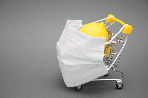 Egy orvosi maszk kerül egy bevásárlókocsira, amely friss citromot tartalmaz.. — Stock Fotó