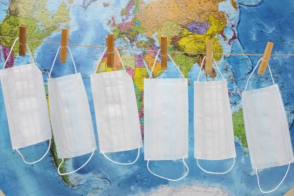 Många medicinska masker hänger på ett rep på klädnypor mot bakgrund av en stor världskarta. Begreppet pandemi. Coronavirus . — Stockfoto