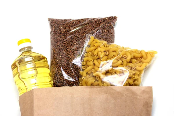Una bottiglia di olio vegetale, grano saraceno e pasta in un sacchetto di carta sono isolati su uno sfondo bianco. Il concetto di donazione  . — Foto Stock