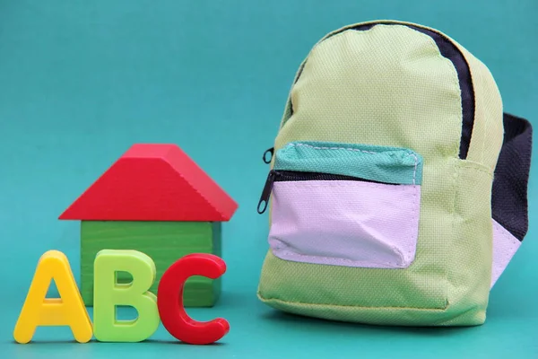 ABC - letters of the English alphabet to the will of a wooden house and a school bag on a green background.