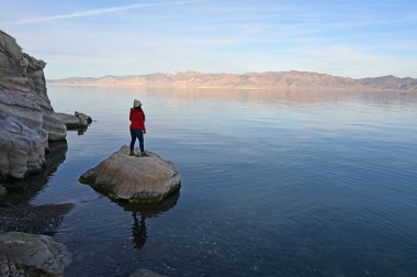Öğleden sonra Nevada 'da, Piramit Gölü kıyısında kayaların üzerinde duran kırmızı kazaklı genç bir kadın..