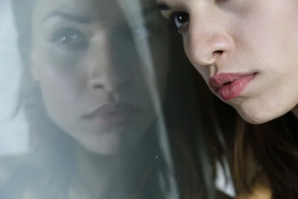 Face of a beautiful young female reflecting in glass surface — Stock fotografie