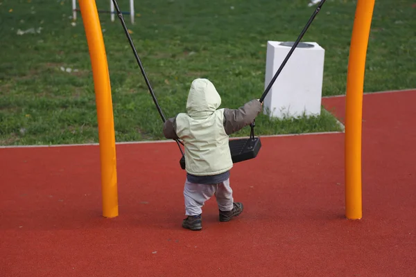 Little boy in autumn jacket swinging on swing — Stock Photo, Image