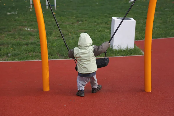 Niño en chaqueta de otoño balanceándose en el columpio — Foto de Stock