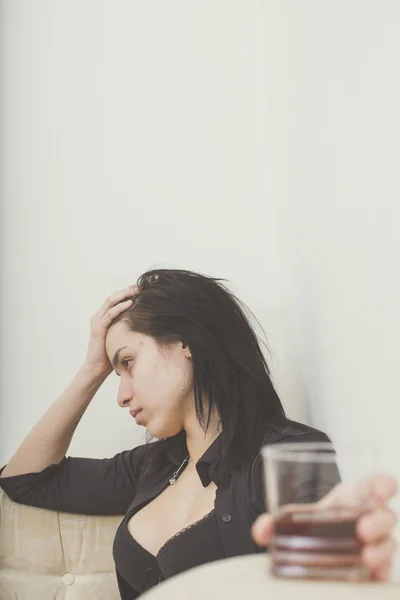 Chica sentada en el sofá en el apartamento y sosteniendo un vaso de alcohol — Foto de Stock