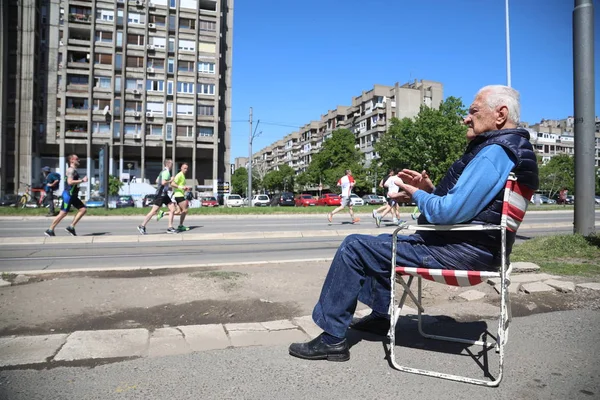 Yaşlı bir adam bir sandalyede oturuyor ve yarışçılar için destek veren — Stok fotoğraf