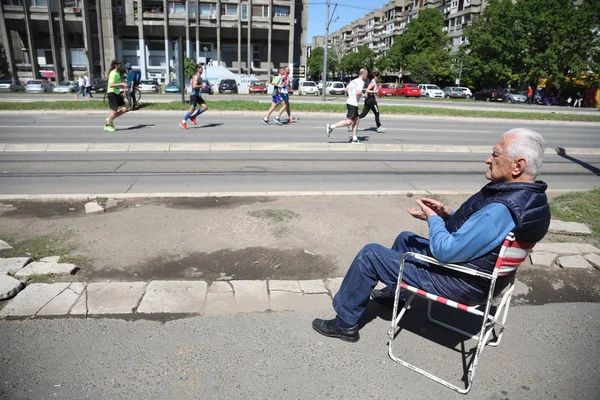 Yaşlı bir adam bir sandalyede oturuyor ve yarışçılar için destek veren — Stok fotoğraf