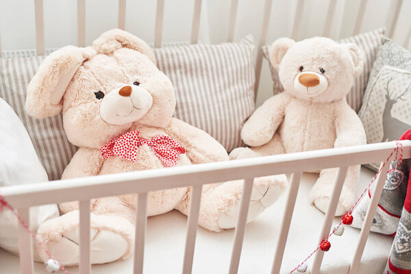 Rabbit and bear in white crib.Soft toys in children 's bedroom. Белая детская комната
.