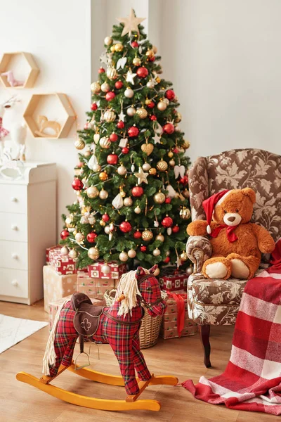 Vánoční interiér dětského pokoje. Nový rok výzdoba a strom v dětském pokoji. Vánoce v dětském pokoji. Houpací kůň a měkké hračky medvěd na pozadí vánočního stromu. — Stock fotografie