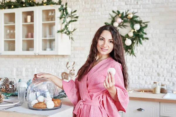 Woman at home for christmas. Woman preparing at home. Smiling woman in pink dress in kitchen. White kitchen interior. Modern kitchen with table and kitchenware. Kitchen in luxury home.