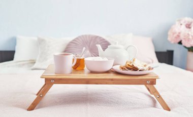 Otel odasında, yatakta kahvaltı. Kalacak yer. Yatakta kahvaltı, çay fincanı, tepside krep ve yatak arkası manzarası. Uzayı kopyala Romantik Sevgililer Günü kahvaltısı. Sıcak kahvaltı Maslenitsa