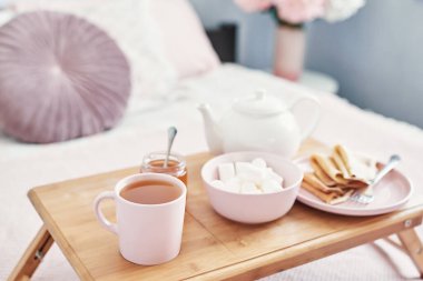 Otel odasında, yatakta kahvaltı. Kalacak yer. Yatakta kahvaltı, çay fincanı, tepside krep ve yatak arkası manzarası. Uzayı kopyala Romantik Sevgililer Günü kahvaltısı. Sıcak kahvaltı Maslenitsa