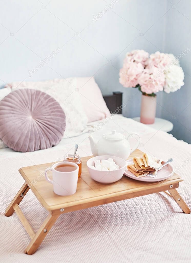 Breakfast in bed in hotel room. Accommodation. Breakfast in bed with tea cup with pancakes on tray on bed background top view. Copy Space. Romantic valentine's day breakfast. Cozy breakfast Maslenitsa