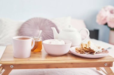 Otel odasında, yatakta kahvaltı. Kalacak yer. Yatakta kahvaltı, çay fincanı, tepside krep ve yatak arkası manzarası. Uzayı kopyala Romantik Sevgililer Günü kahvaltısı. Sıcak kahvaltı Maslenitsa