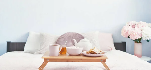 Breakfast in bed in hotel room. Accommodation. Breakfast in bed with tea cup with pancakes on tray on bed background top view. Copy Space. Romantic valentine\'s day breakfast. Cozy breakfast Maslenitsa