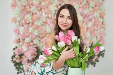 Çiçek arkaplanda lale çiçekleri olan güzel bir kız. 8 Mart Kadınlar Günü ya da Anneler Günü için tebrik kartı. Çok hoş bir çiçekçi kadın elinde çiçek buketi tutuyor..