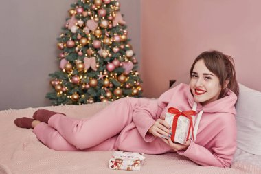 Mutlu Noeller ve mutlu tatiller! Noel tebrik kartı şablonu. Tatiller, kutlamalar, aile ve insanlar konsepti - oturma odası üzerinde hediye kutusu olan mutlu kız ve Noel ağacı arka planı.