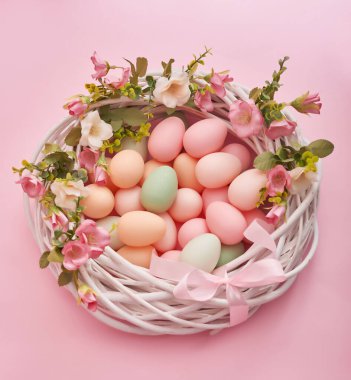 Renkli paskalya yumurtaları pastel arka planda çiçeklerle birlikte, kopyalama alanı. Paskalya süsleri. Yuvasında boyanmış yumurtalar olan paskalya arkaplanı, klasik tarz, üst manzara. Bahar tebrik kartı..