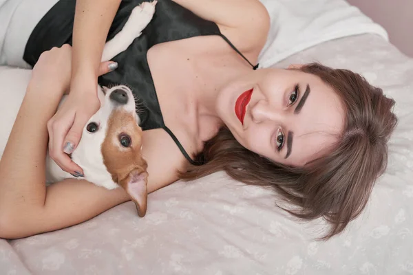 Girl and dog in bed. Beautiful woman in pajamas sits on bed in bedroom with dog Jack Russell Terrier, enjoys morning weekend, has good relationship with pet. Man best friend dog. Cozy morning.