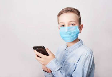 Cep telefonlu tıbbi maskeli bir çocuk. Coronavirus ve Hava kirliliği pm2.5 konsepti. Virüs belirtileri. Salgın, grip, hastalıklardan korunma, aşı kavramı. Grip hastalığı. Tıbbi bakım