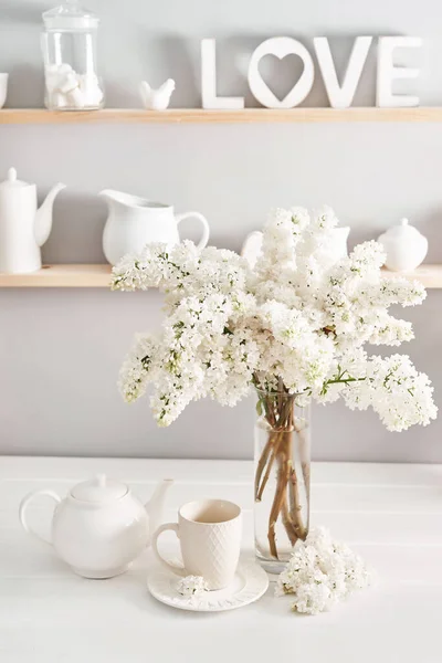 Bouquet of white lilac in vase and tea set on table in kitchen. Happy birthday greeting card. Hello spring and summer. Greeting card for Women\'s Day and Mother\'s Day. Spring season, copy space.