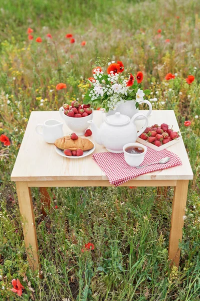 Romantic Valentines french or rural breakfast: tea, strawberries, croissants on table in poppy field. Countryside and Cozy Good morning weekend concept. Background with copy space. Date outdoors