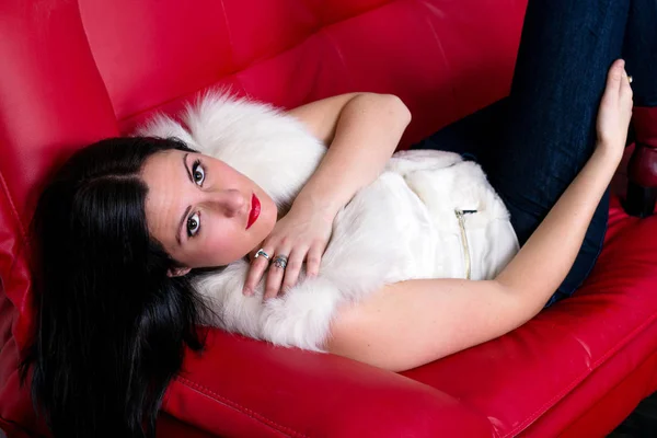 Luxurious young women model on red couch — Stock Photo, Image