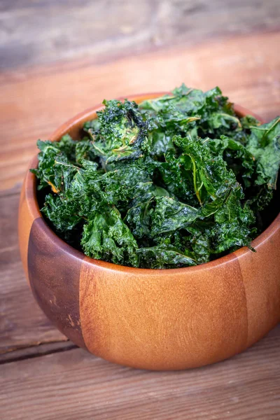 Healthy homemade seasoned green kale chips snack on a wooden bowl over a plank table — Stock Image Healthy Homemade Seasoned Green Kale Chips Snack Wooden Bowl Plank Stock Picture