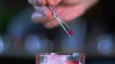 Birisi kokteyle çiçek koyuyor. Barmen barda kokteyl hazırlıyor. Alkollü kokteyl yapma süreci. Ağır çekimde yakın çekim