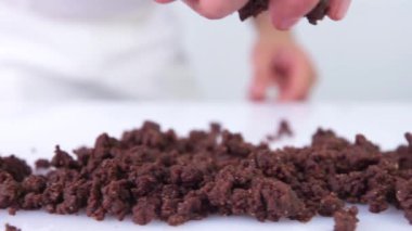 Pasta şefi beyaz bir masaya çikolata parçacıkları atıyor. Çikolata yavaş çekimde beyaz arka plana düşer. Birisi tatlı yapıyor..