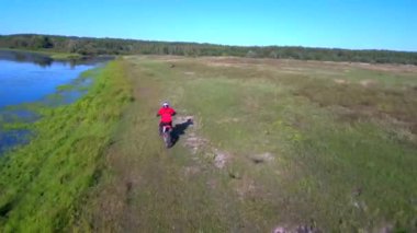 Adam yazın bir spor bisikleti sürüyor. Göl kenarında.