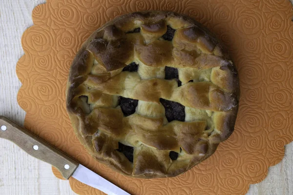 Tarte à la confiture de pommes remplie de cerises et de noix et un couteau couché sur une table en bois — Photo