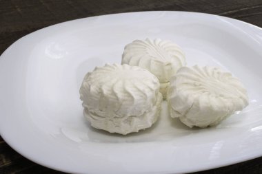 Kahverengi ahşap masadaki beyaz seramik tabakta taze beyaz marşmelov.