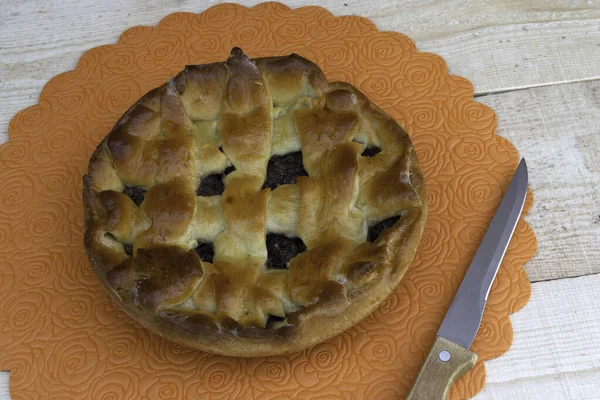 Appeltaart gevuld met kersen en walnoten en een mes op een houten tafel — Stockfoto