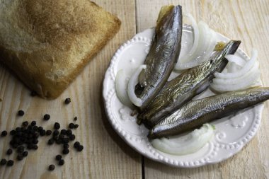 Tabakta tütsülenmiş kapelinler ahşap masada bir parça ekmek ve biberle duruyor.