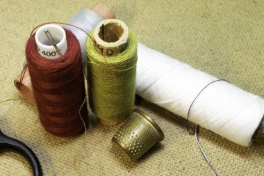 İplikler, iğneler, yüksük ve makas masanın üstünde.