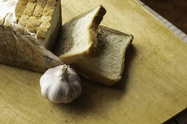 a loaf of sliced bread and a head of garlic lie on the cutting board