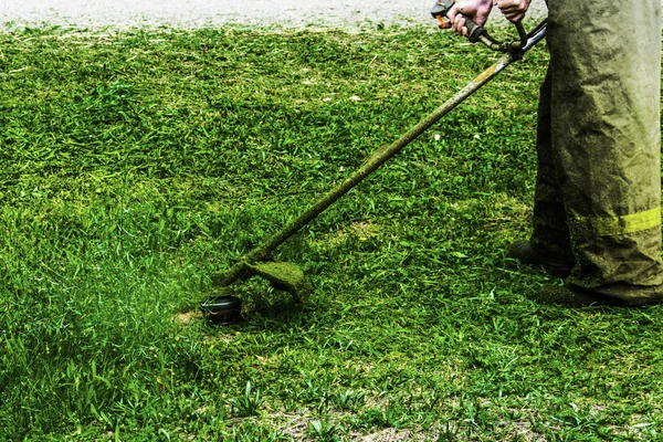 Hombre en ropa de trabajo siega hierba verde con un trimmer —  Fotos de Stock