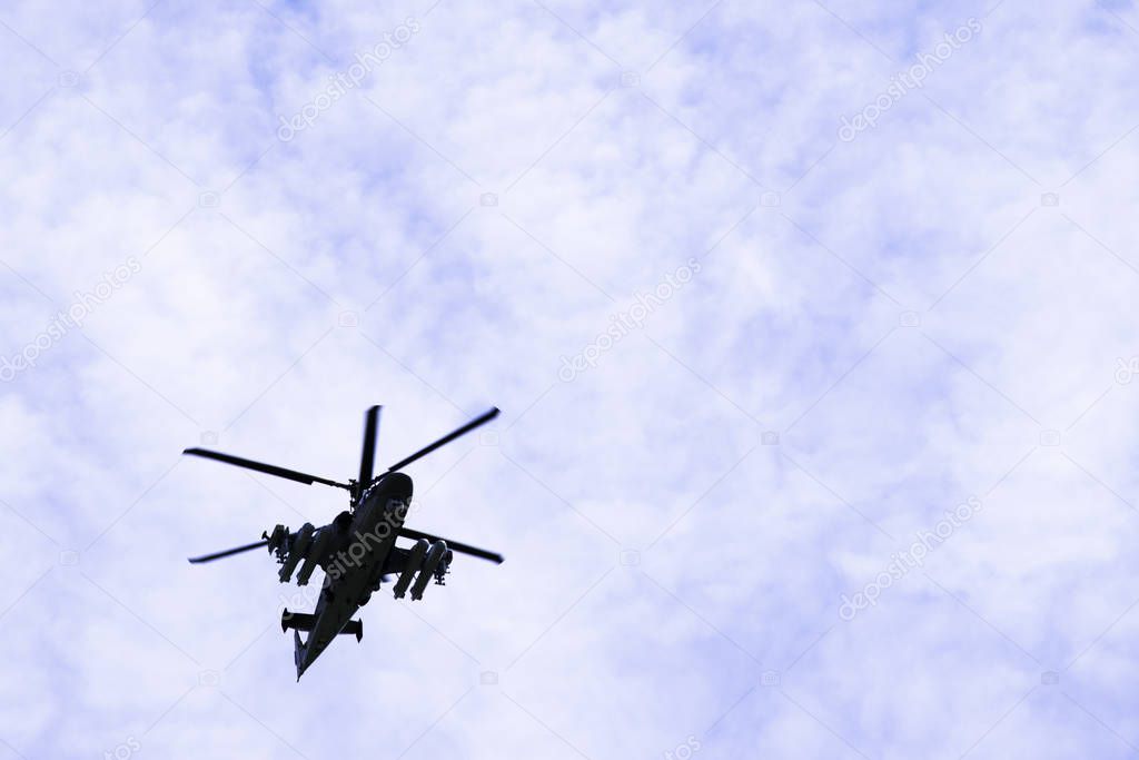 Russian military combat attack helicopter K-52 Alligator flies against a blue sky and clouds