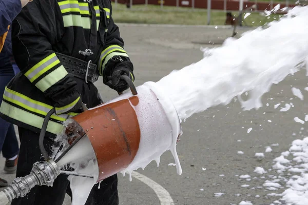 Supply of foam from a foam generator, fire extinguishing foam flies from the foam generator, which keeps the fireman in combat clothing — Stock Photo, Image