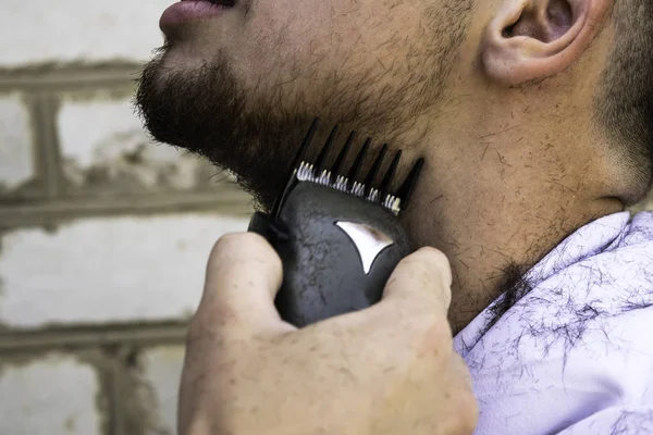 the barber cuts his beard to a guy with a shearing machine