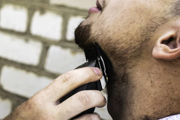 the barber cuts his beard to a guy with a shearing machine