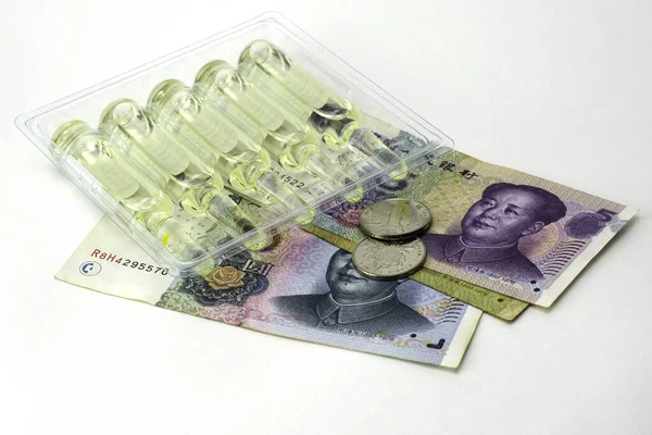 Koncepce vakcinace a léčba coronovirus v porcelánu ampulky s léky a čínské peníze juanů na bílém pozadí — Stock fotografie
