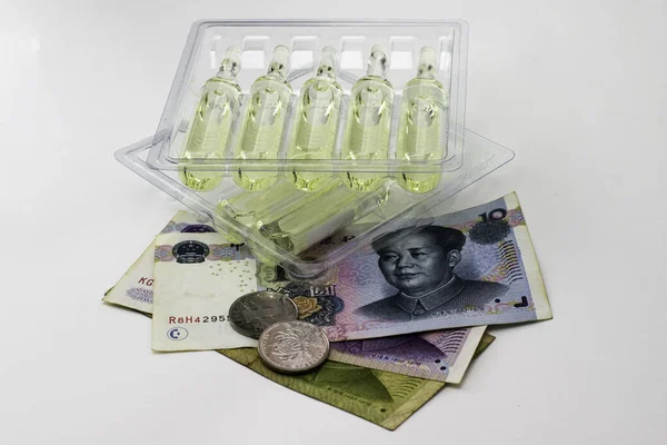 Koncepce vakcinace a léčba coronovirus v porcelánu ampulky s léky a čínské peníze juanů na bílém pozadí — Stock fotografie