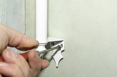 Bir adamın eli kapıya tornavidayla beyaz bir metal sapı vidalıyor.