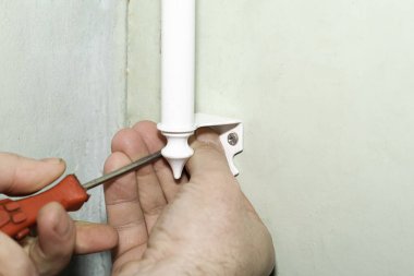 Bir adamın eli kapıya tornavidayla beyaz bir metal sapı vidalıyor.