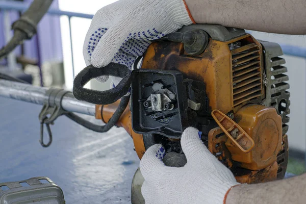 Un maestro en guantes de trabajo repara el motor de la vieja recortadora de gas elimina el elemento filtrante del filtro de aire — Foto de Stock